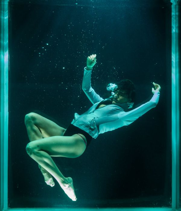 Woman performing a fluid cardio movement in a dark studio with neon blue highlights.